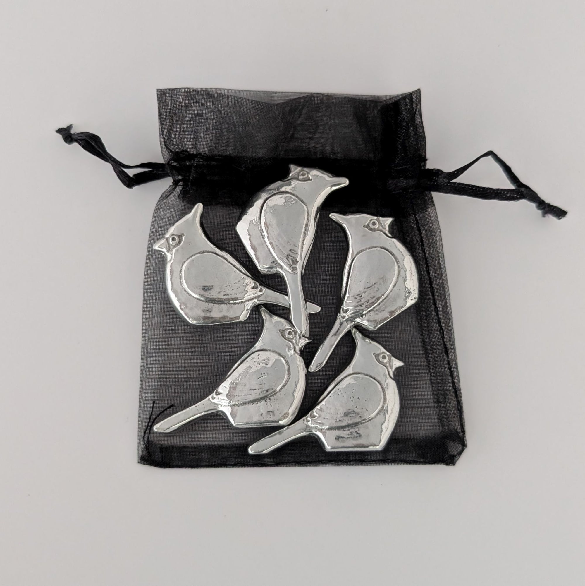 Silver bird-shaped objects in a black drawstring bag on a light gray background