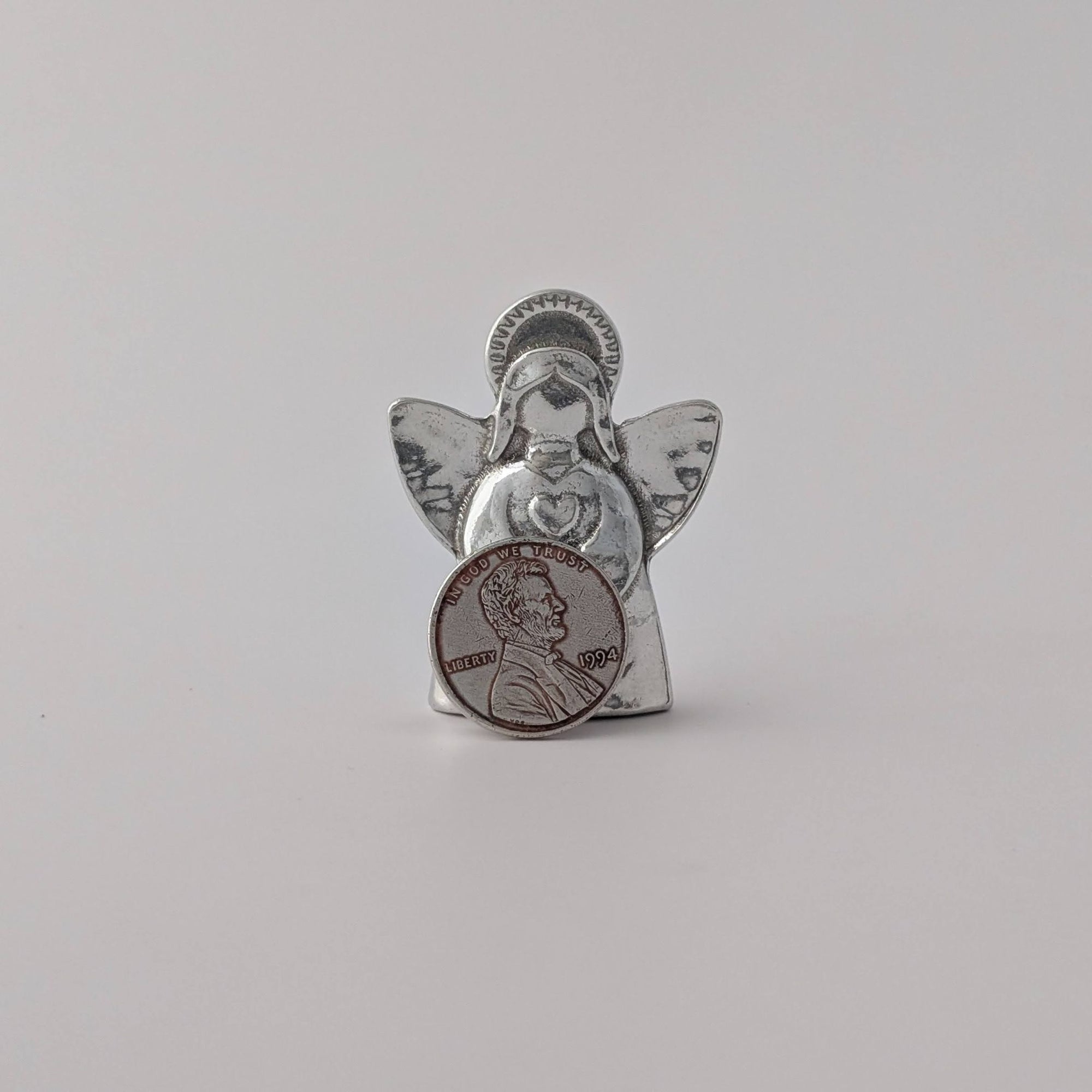 Silver angel figurine holding a penny on a light gray background