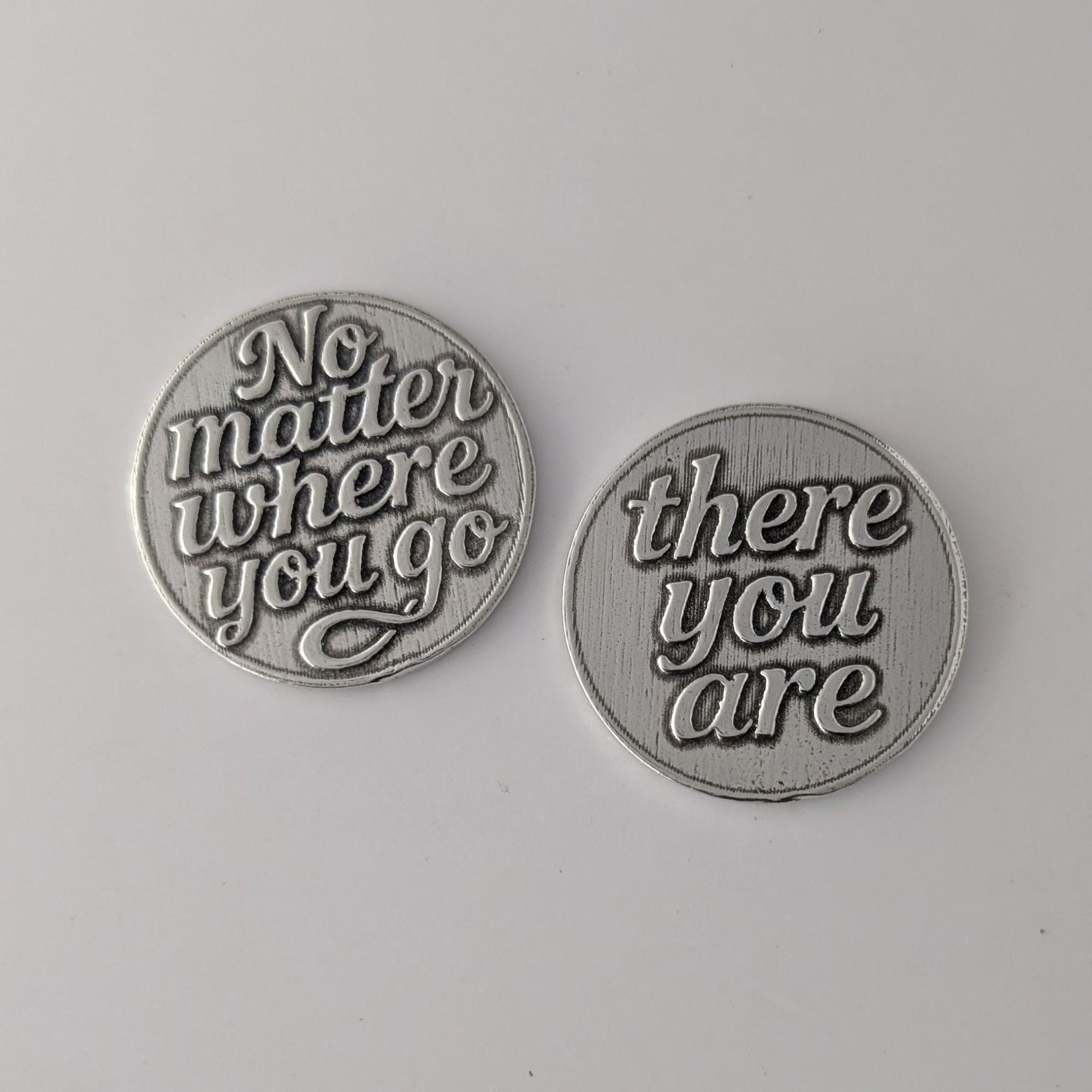 Two pewter tokens with engraved text on a gray background