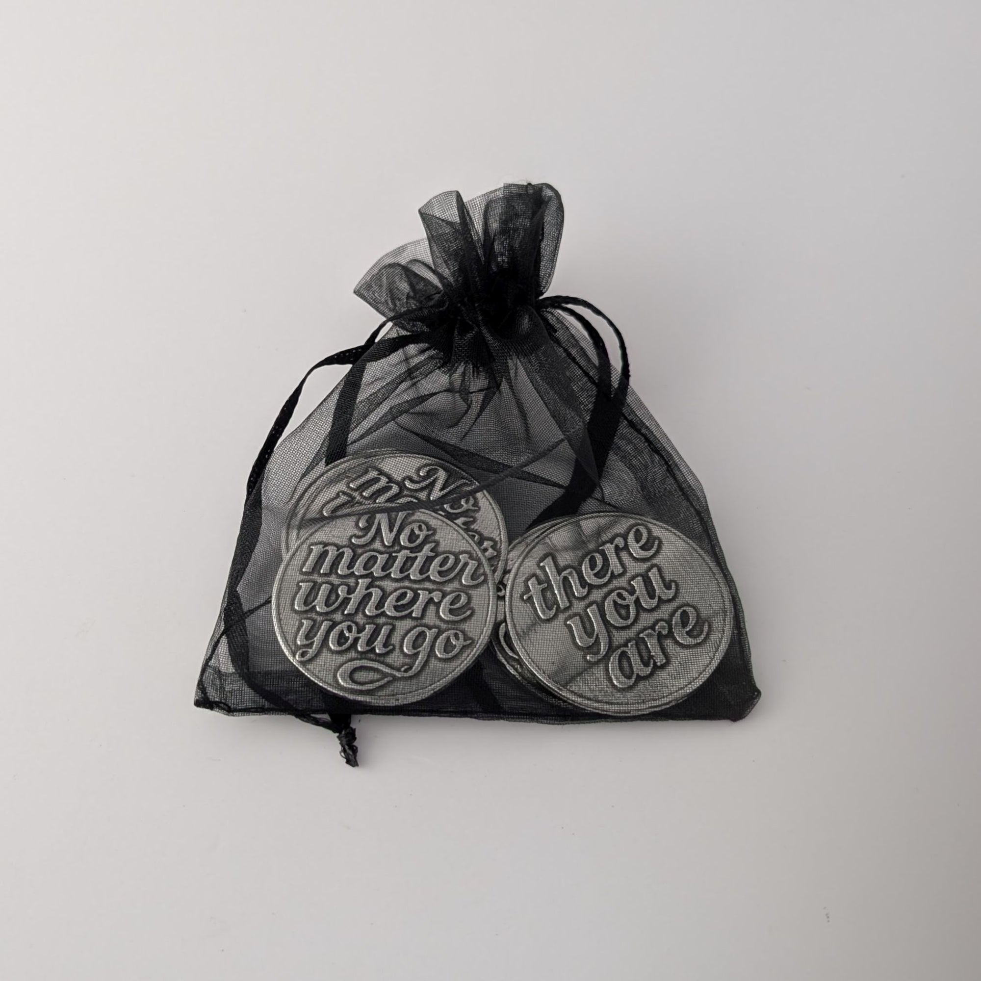 Pewter coins with engraved text in a black drawstring bag on a white background