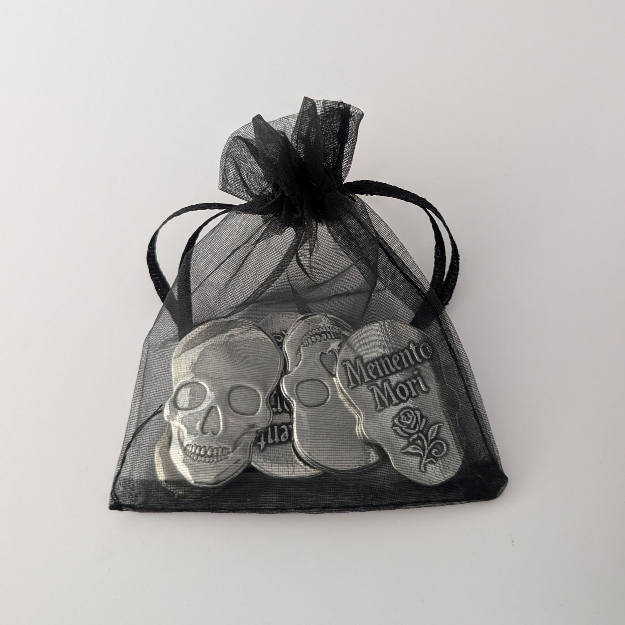 Silver skull-shaped pendants in a black drawstring bag on a white background