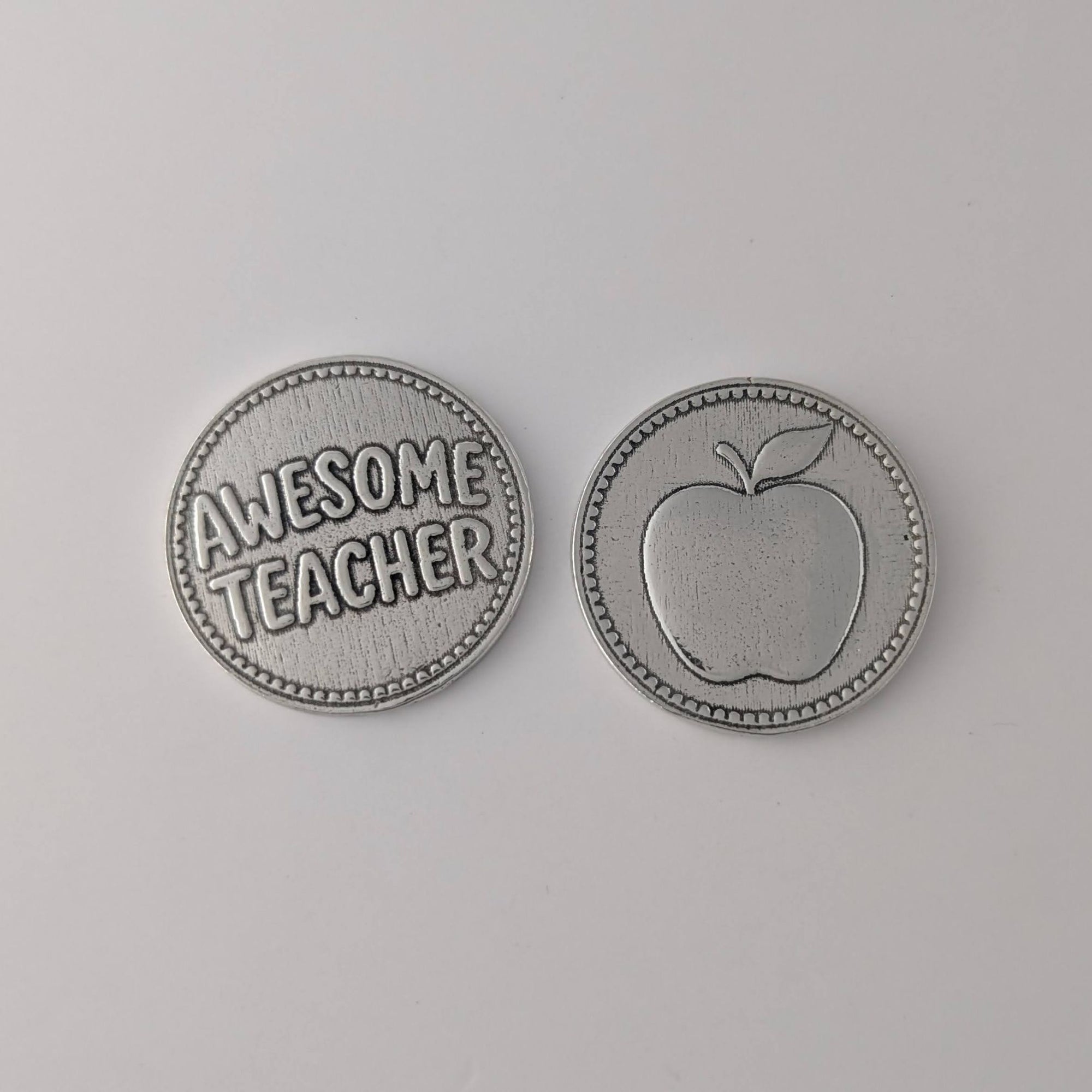 Two pewter coins on a gray background, one with 'Awesome Teacher' text and the other with an apple design.