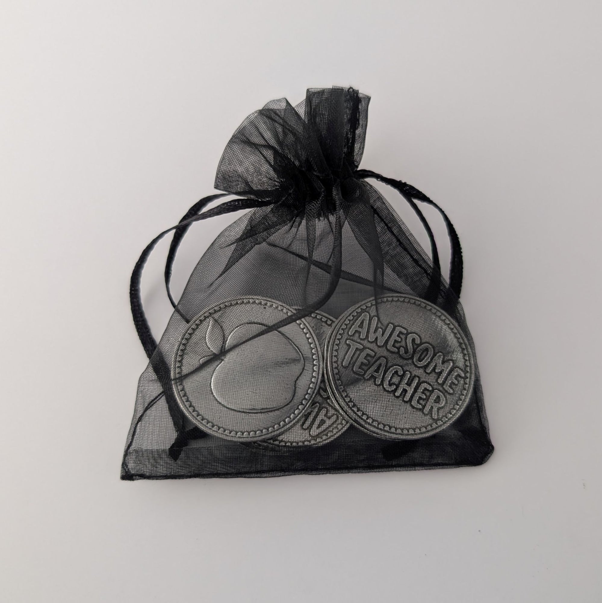 Pewter coins with 'Awesome Teacher' and an apple design in a black organza bag on a light gray background.