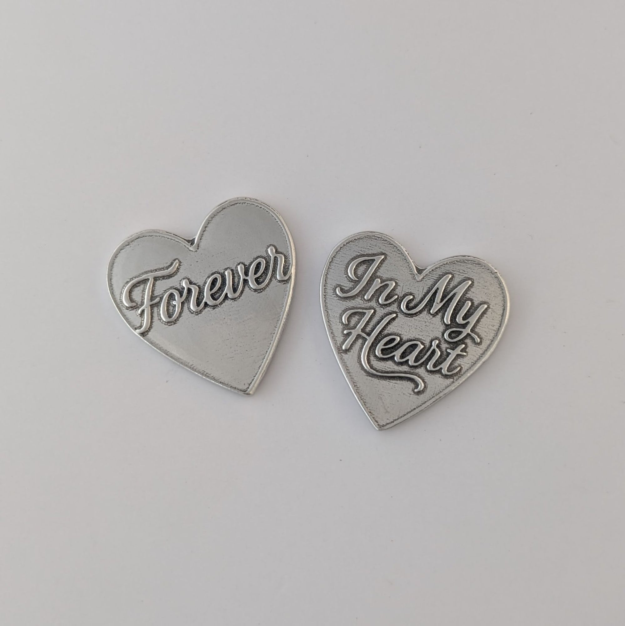 Two silver heart-shaped pendants with engraved text on a light gray background