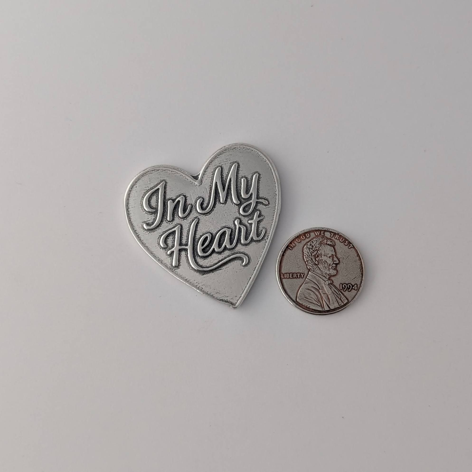 Heart-shaped metal badge with 'In My Heart' text next to a penny on a light gray background