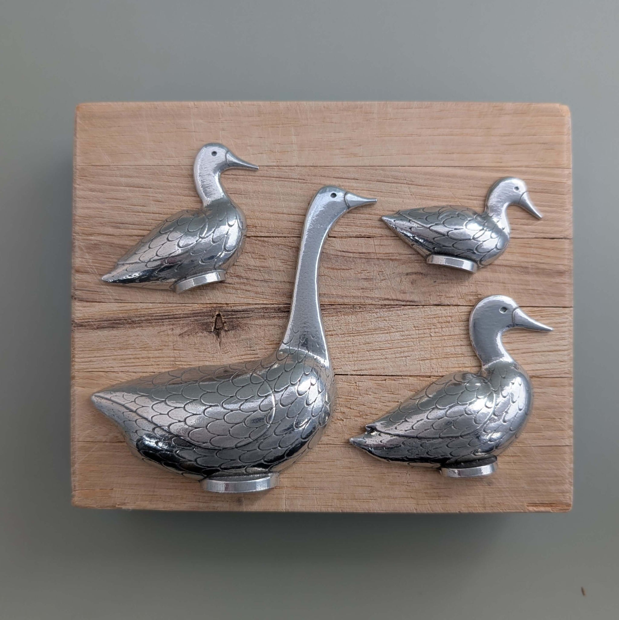 Goose and duck pewter measuring spoons on wooden board