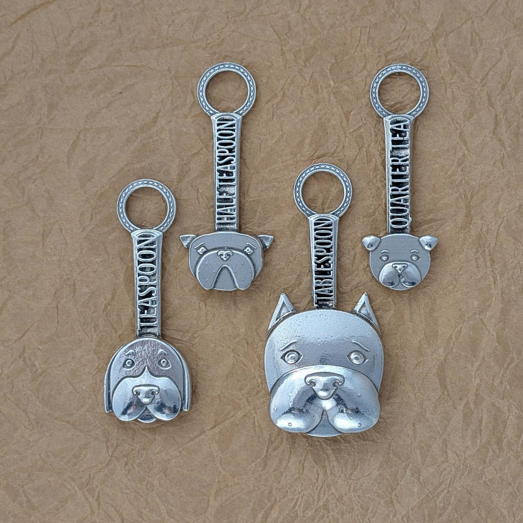 Pewter dog measuring spoons on brown surface