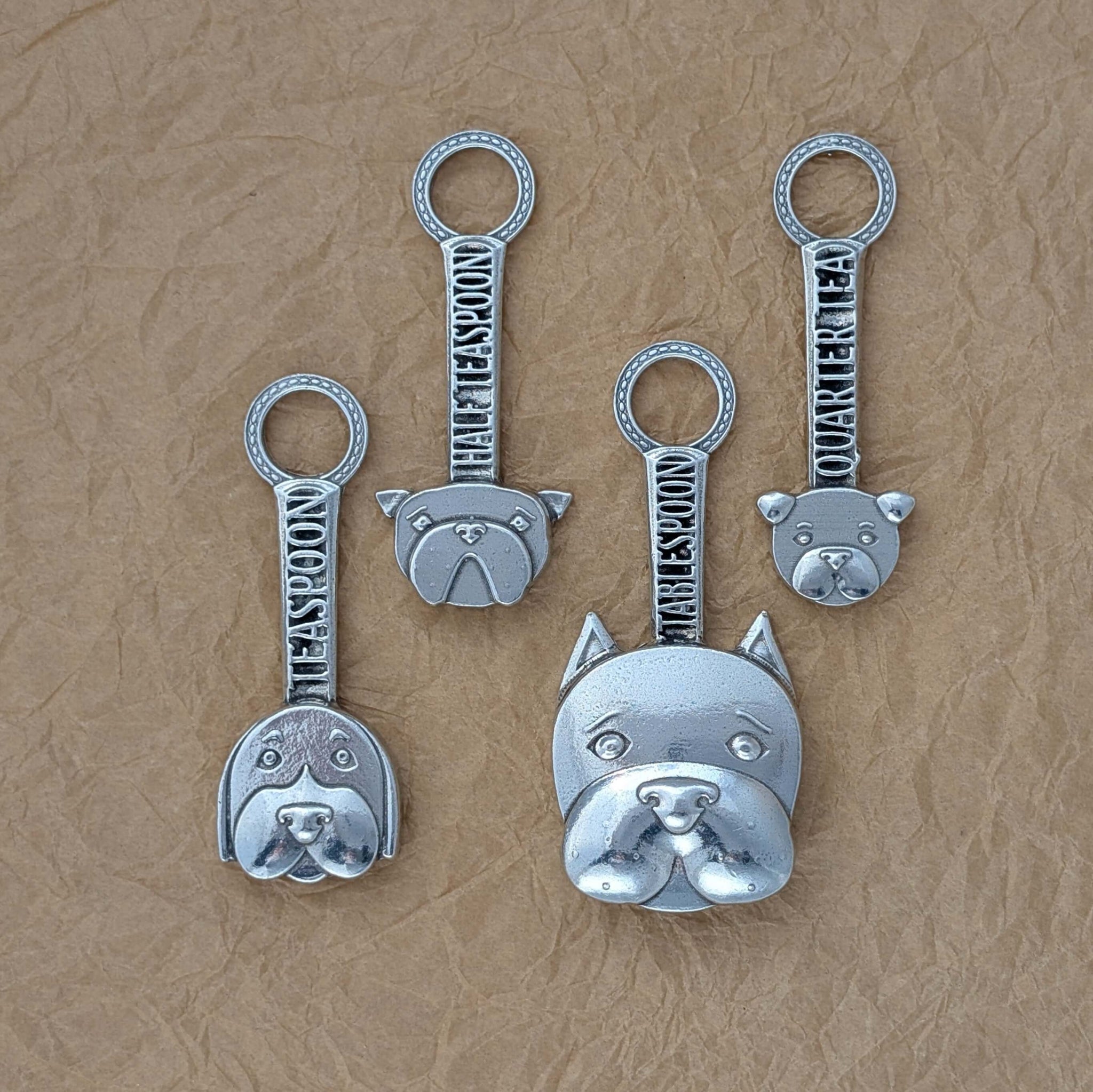 Pewter dog measuring spoons on brown surface