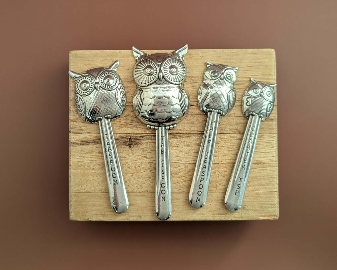 Pewter owl measuring spoons on wood