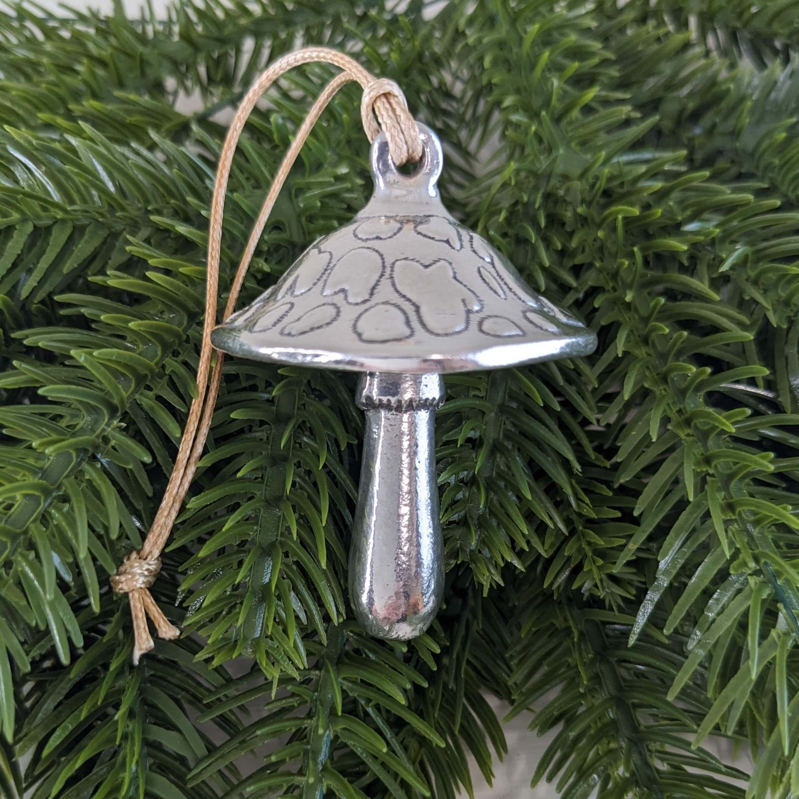A handcrafted pewter mushroom ornament with a classic silhouette, featuring a softly sculpted cap and stem, displayed against a festive green background.