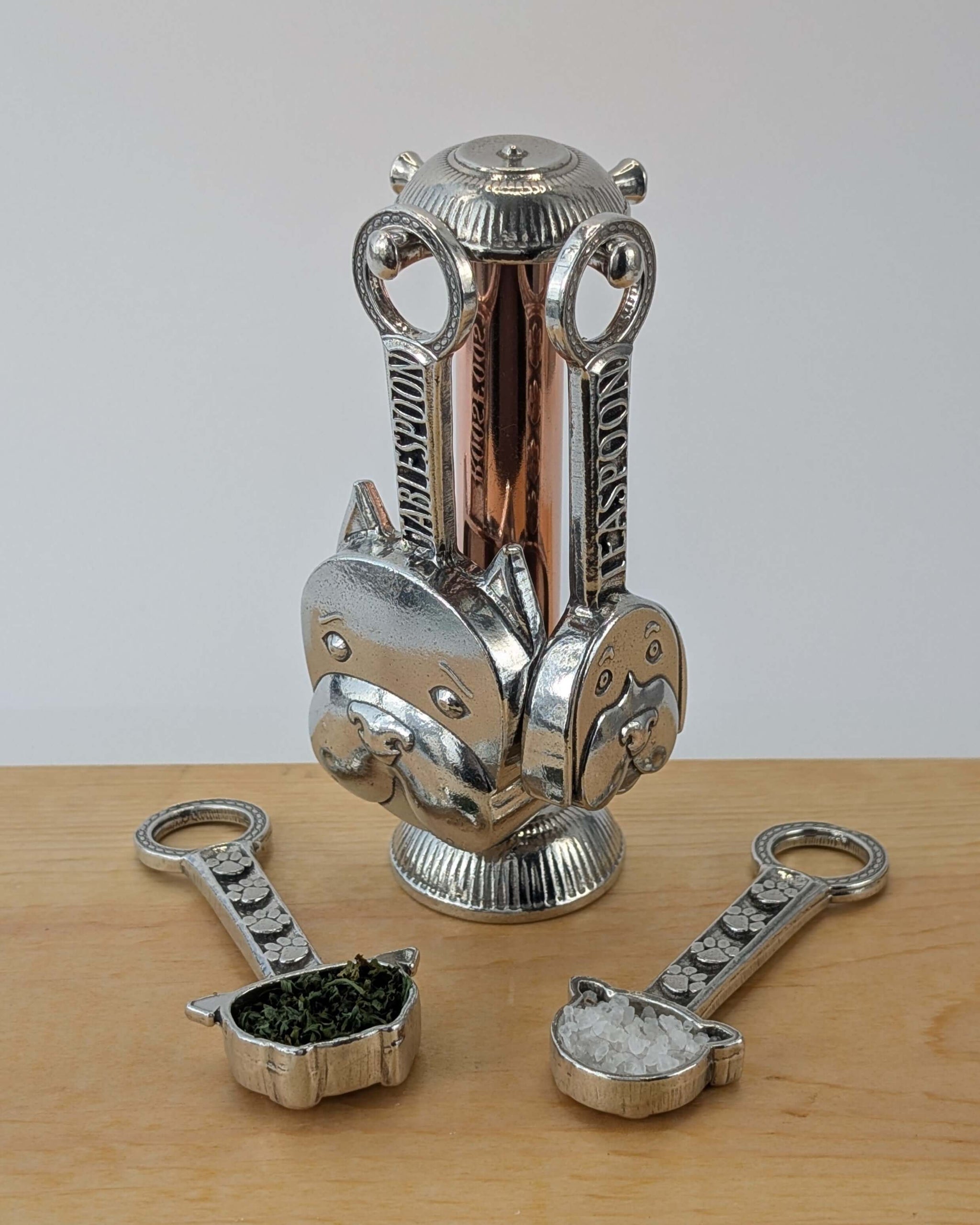 Pewter dog measuring spoons with  copper stand on wooden surface
