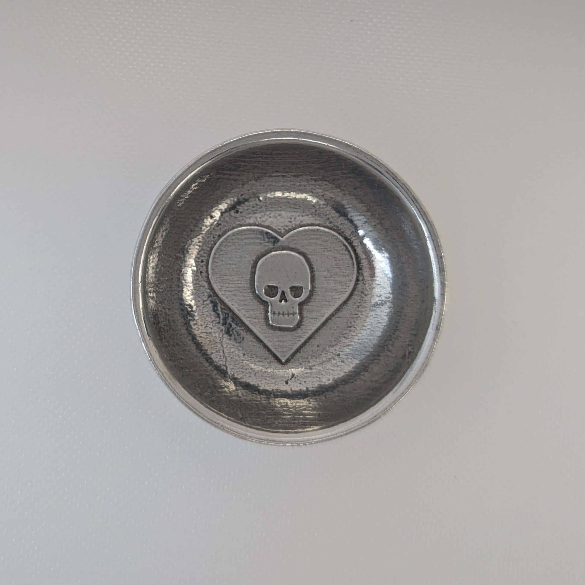 Skull in heart pewter ring dish on white surface.