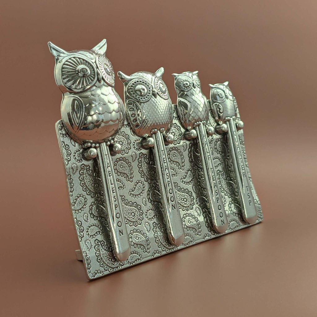 Pewter owl measuring spoons on brown background