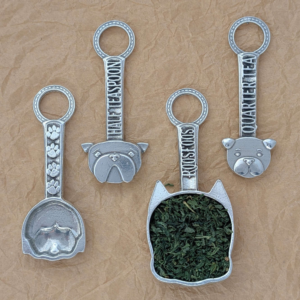Pewter dog measuring spoons on brown surface