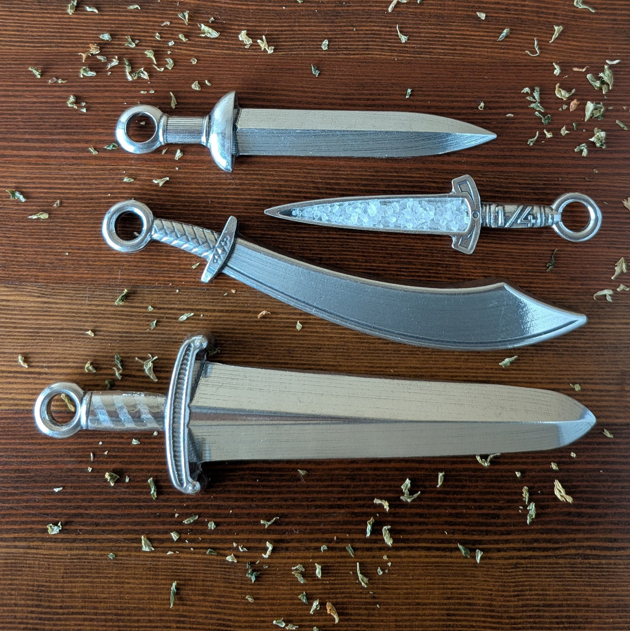 Three silver dagger models on a wooden surface with scattered leaves.
