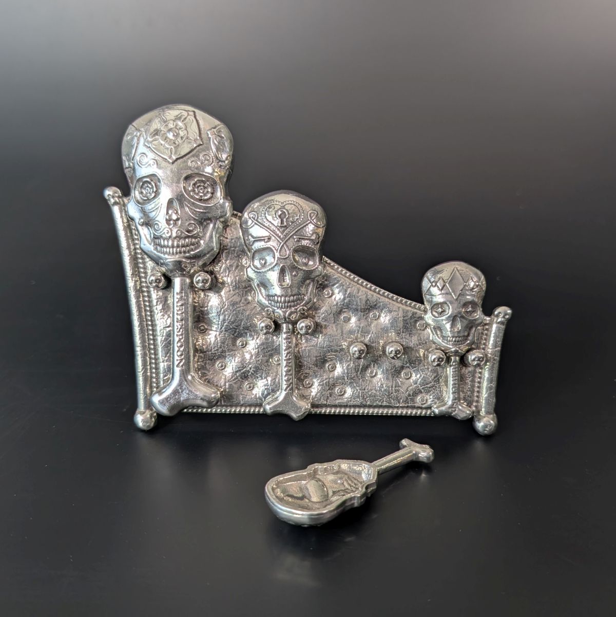 Pewter skull measuring spoons on display stand. Black background.