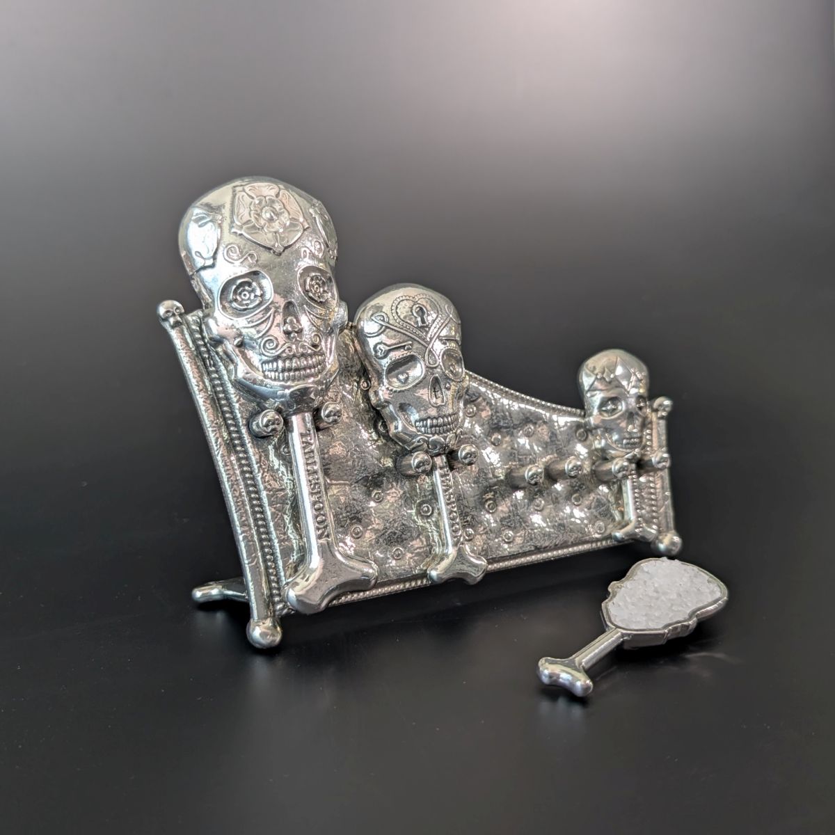 Pewter skull measuring spoons on display stand. Black background