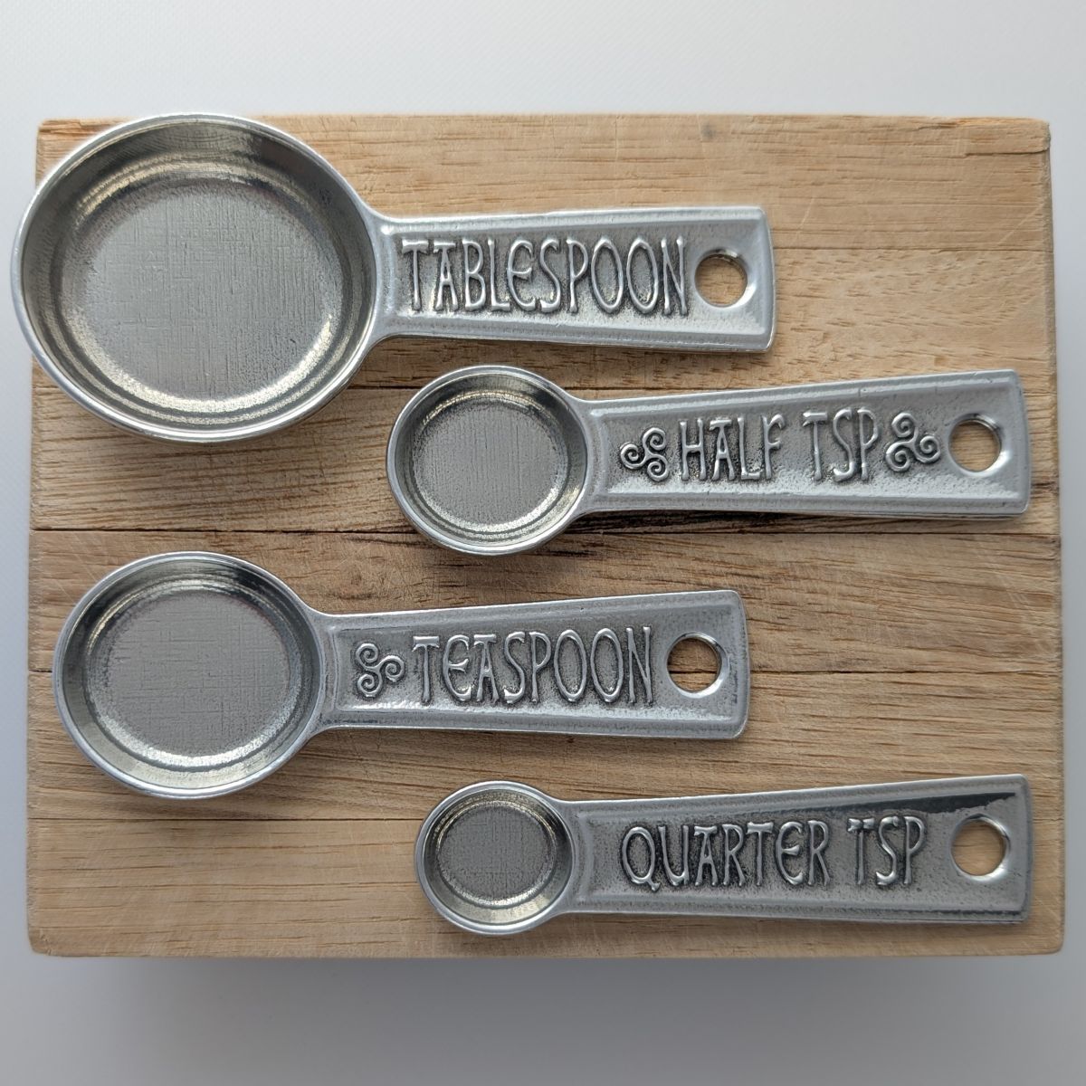 Set of metal measuring spoons with engraved measurements on a wooden board