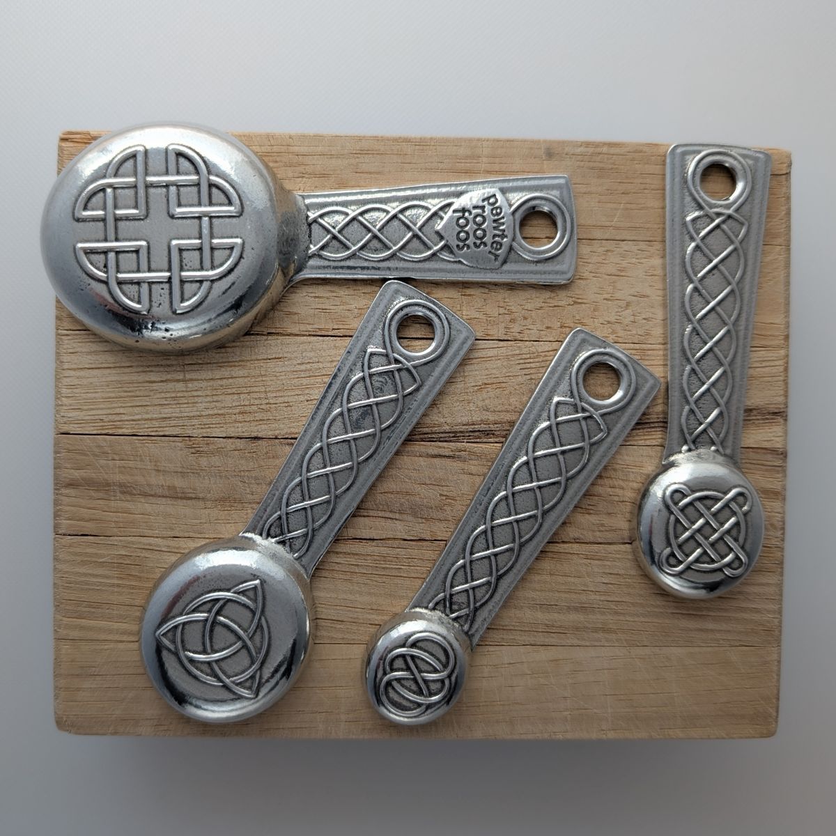Set of silver measuring spoons with Celtic knot designs on a wooden board