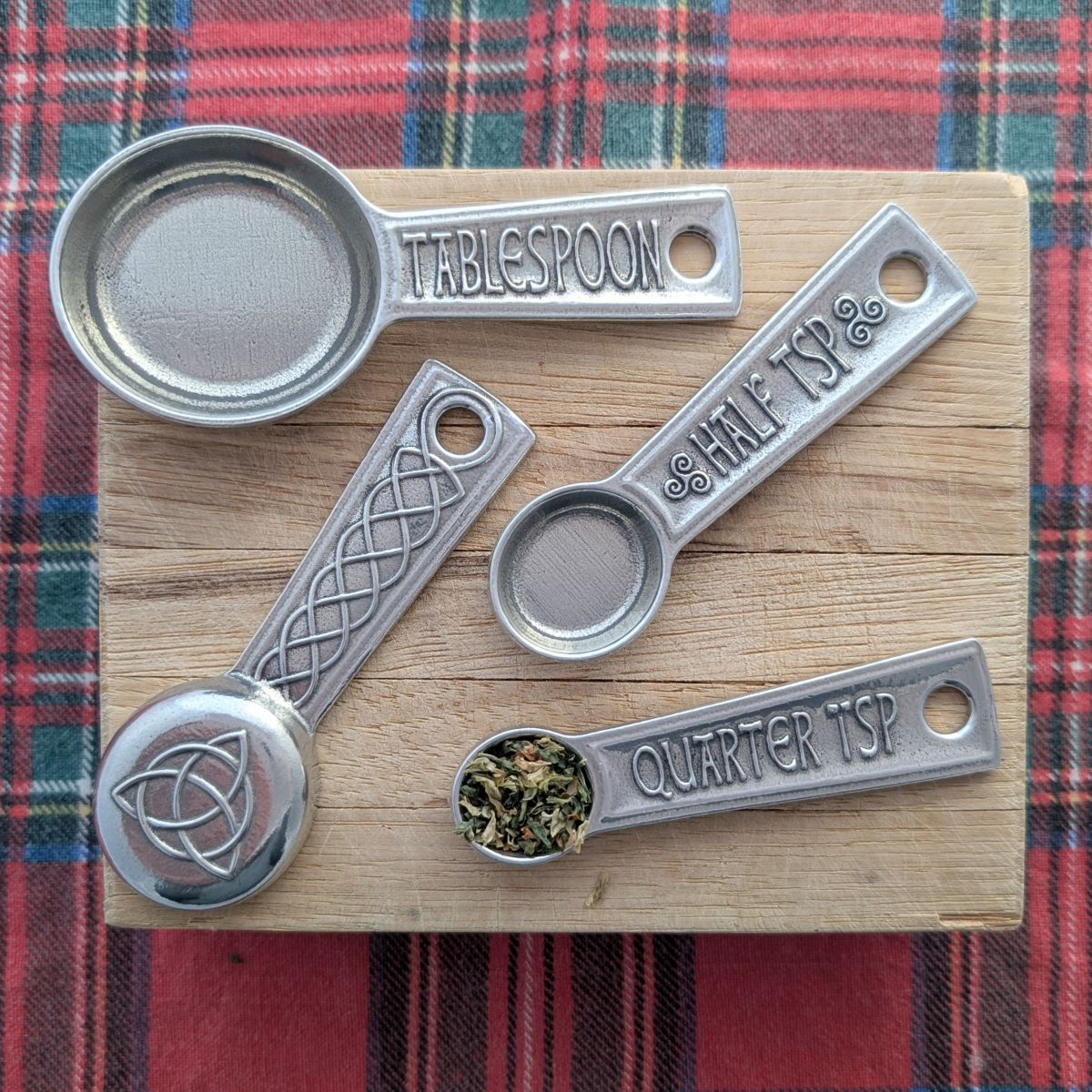 Set of pewter measuring spoons on a wooden board with a plaid background