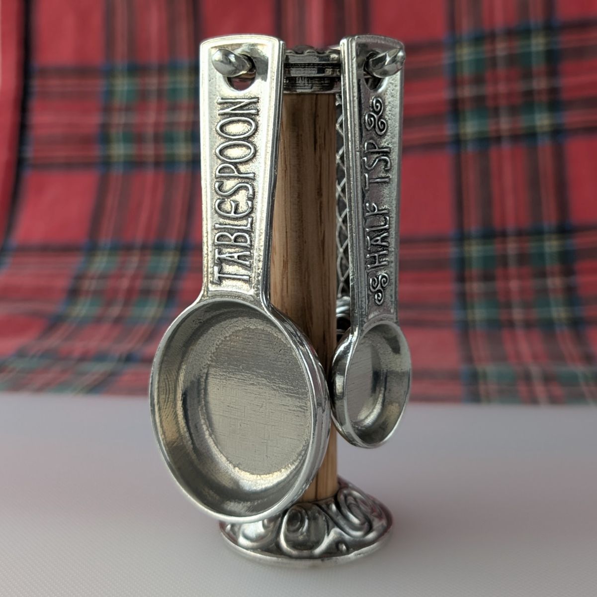Metallic measuring spoons with 'Tablespoon' and 'Half Tbsp' markings on a plaid fabric background.