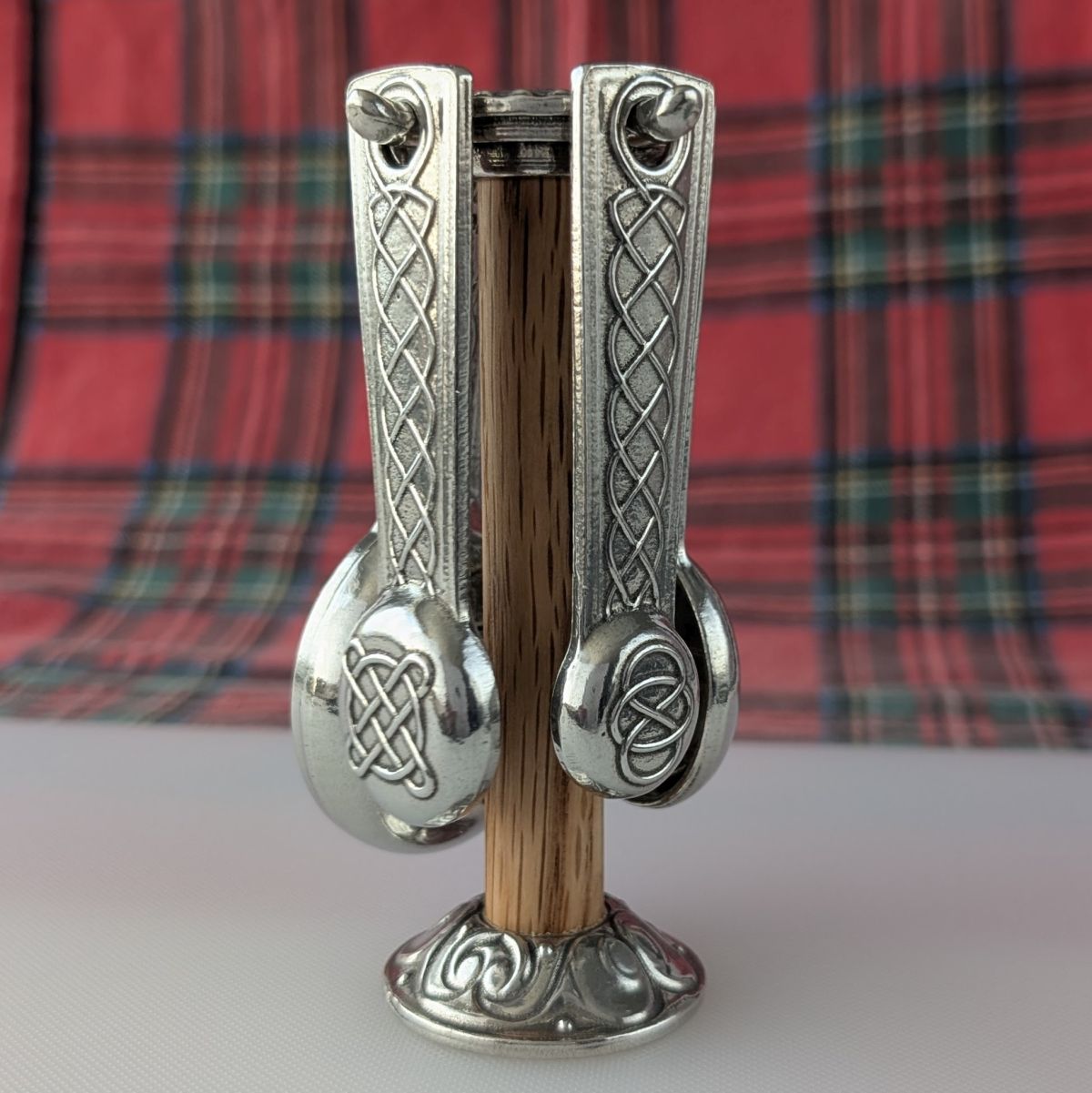Decorative metal and wooden object with Celtic knot designs on a plaid fabric background