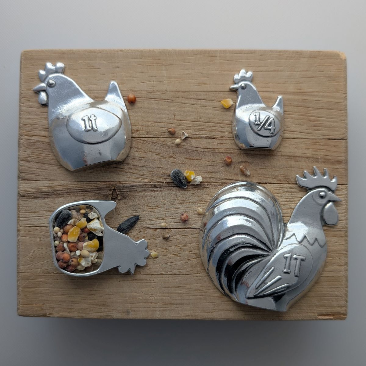 Set of four metal chicken-shaped bird spoons on a wooden surface.
