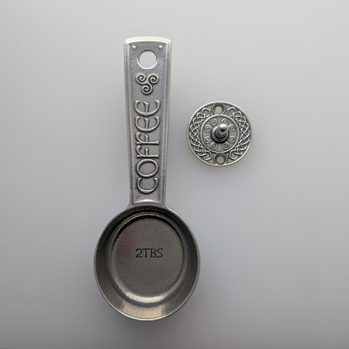 Metallic coffee scoop with 'COFFEE' and '2TBS' text on a light gray background