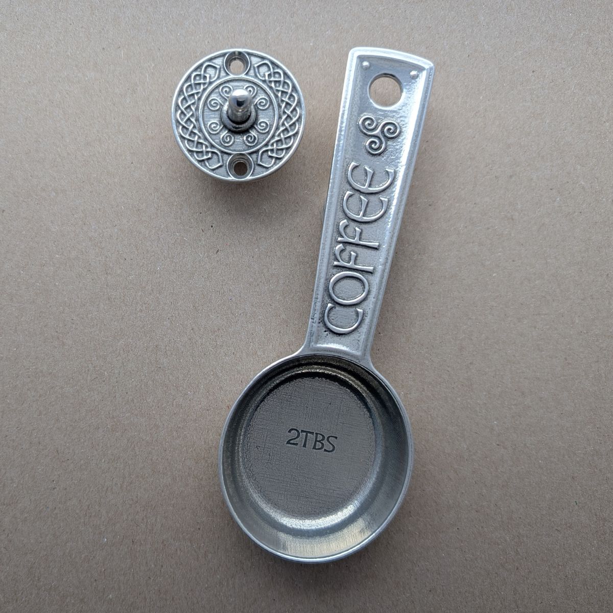 Metallic coffee scoop with 'COFFEE' and '2TBS' text on a brown background