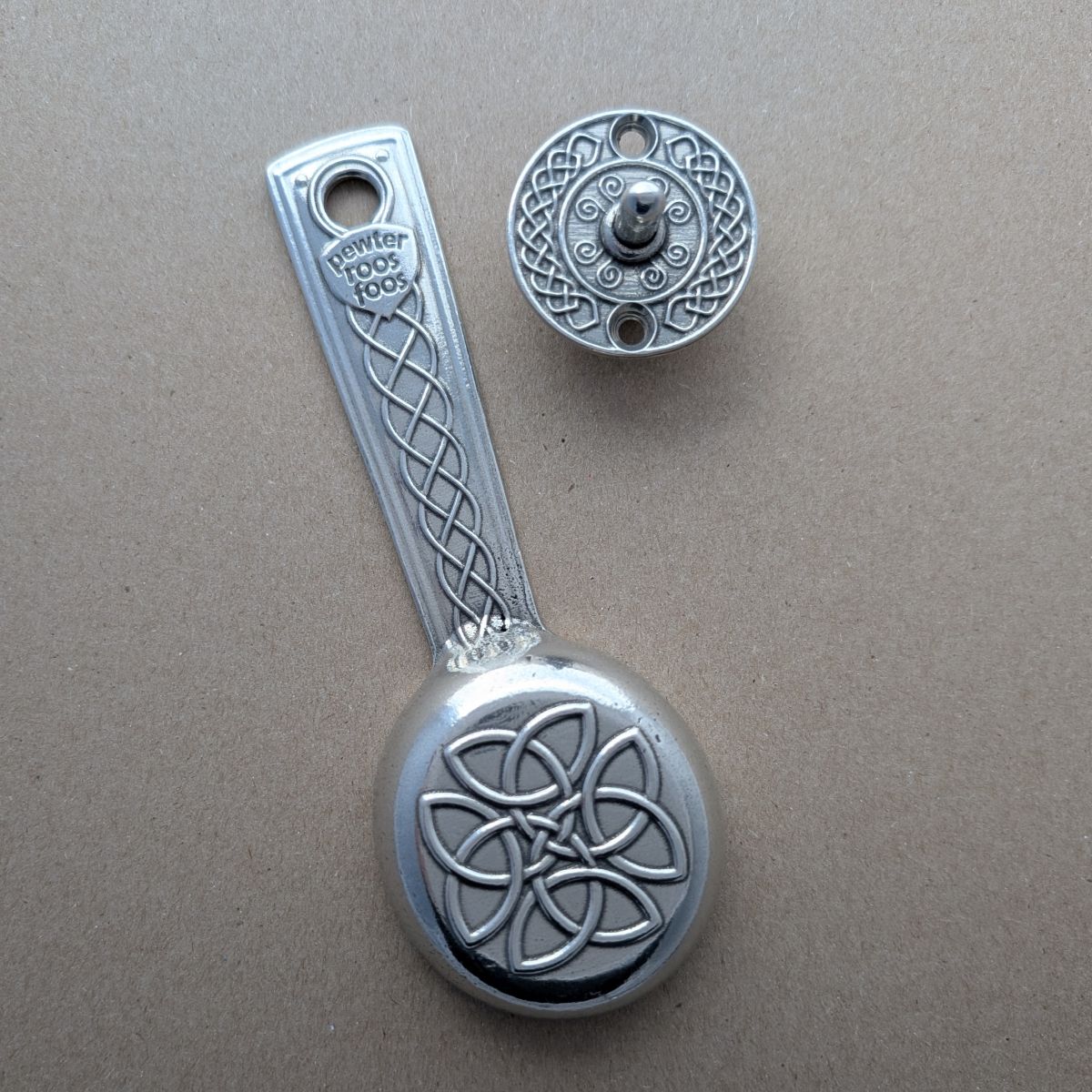 Silver decorative spoon and knob with Celtic knot design on a beige background