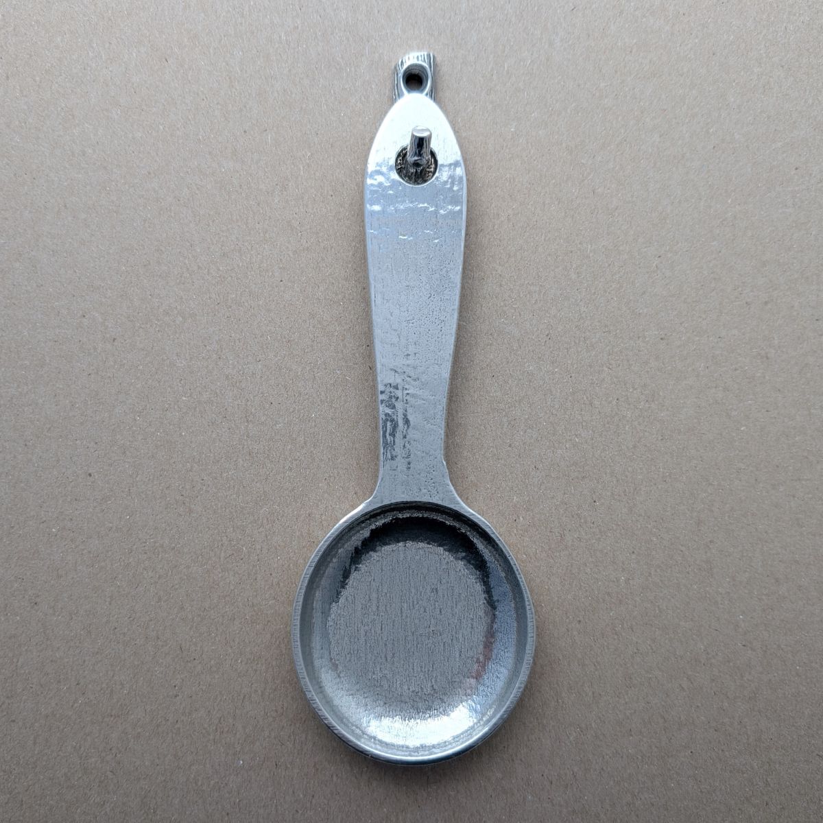 Pewter coffee scoop hanging on hook on brown background