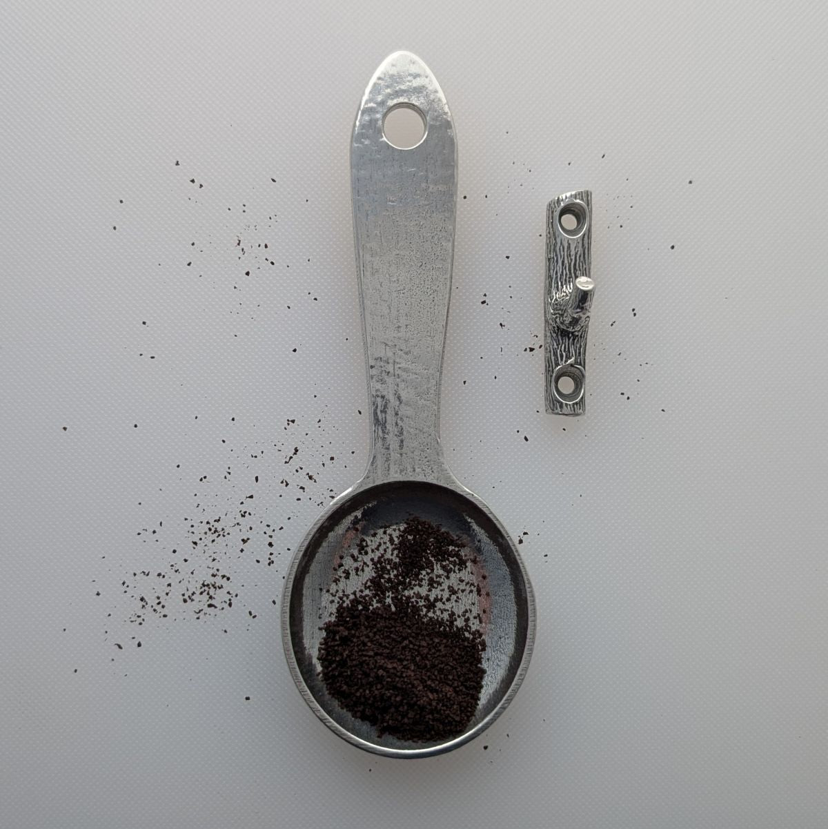 Pewter coffee scoop with coffee and branch hook on white background