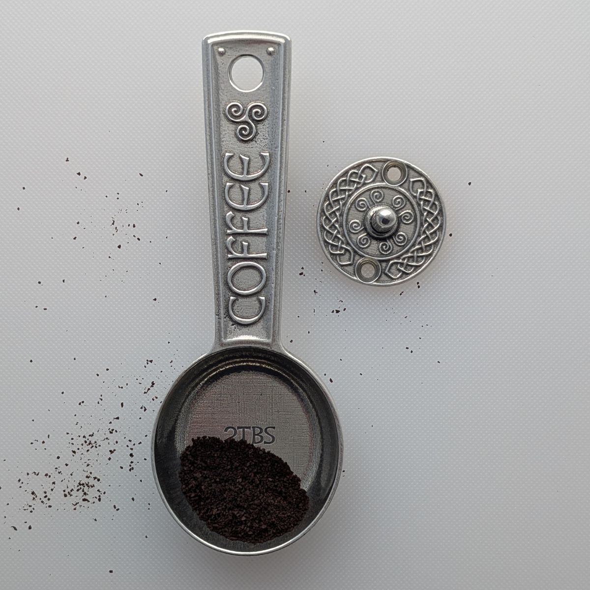 Pewter coffee scoop with 'COFFEE' text on a light gray background