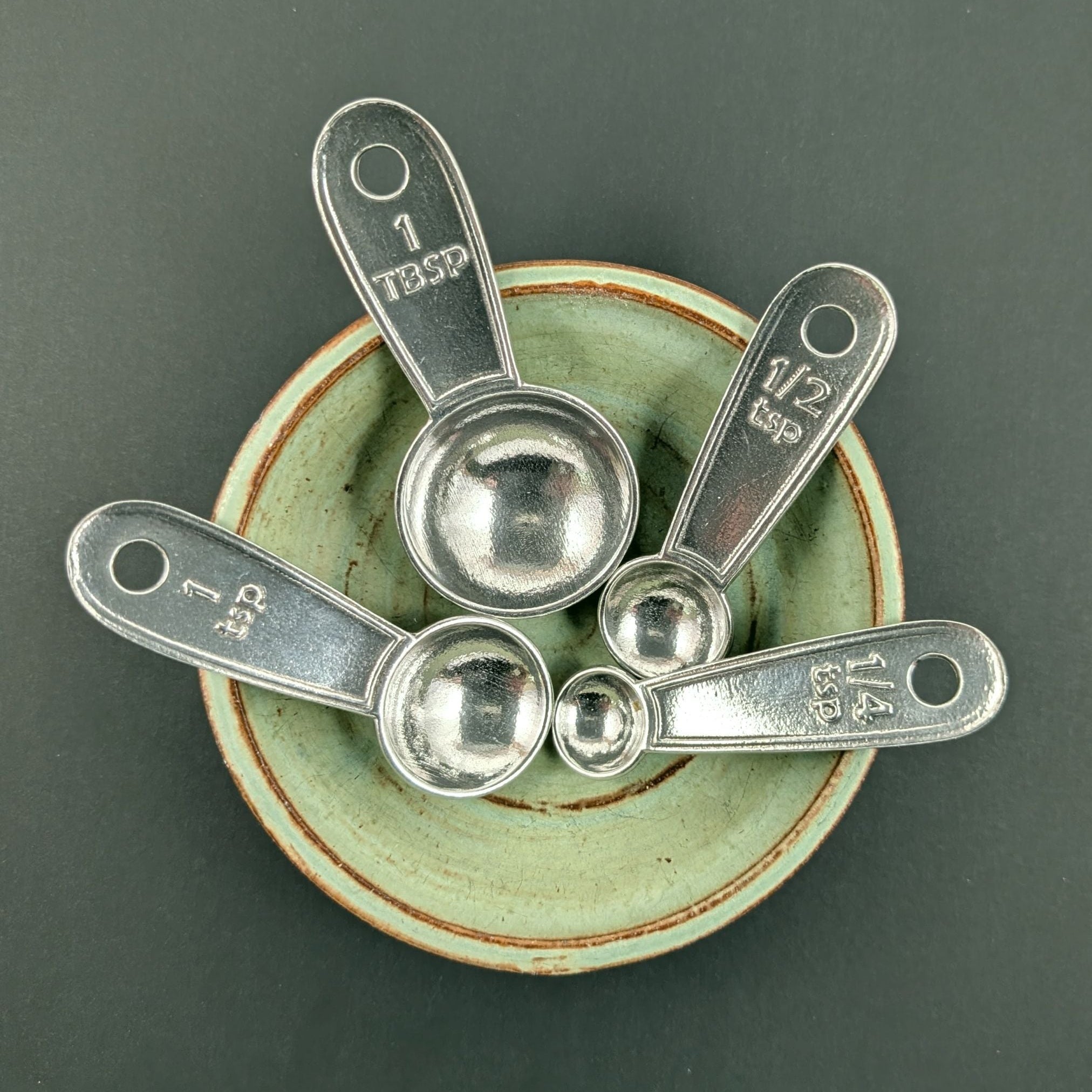 Set of silver measuring spoons on a ceramic dish with a dark background