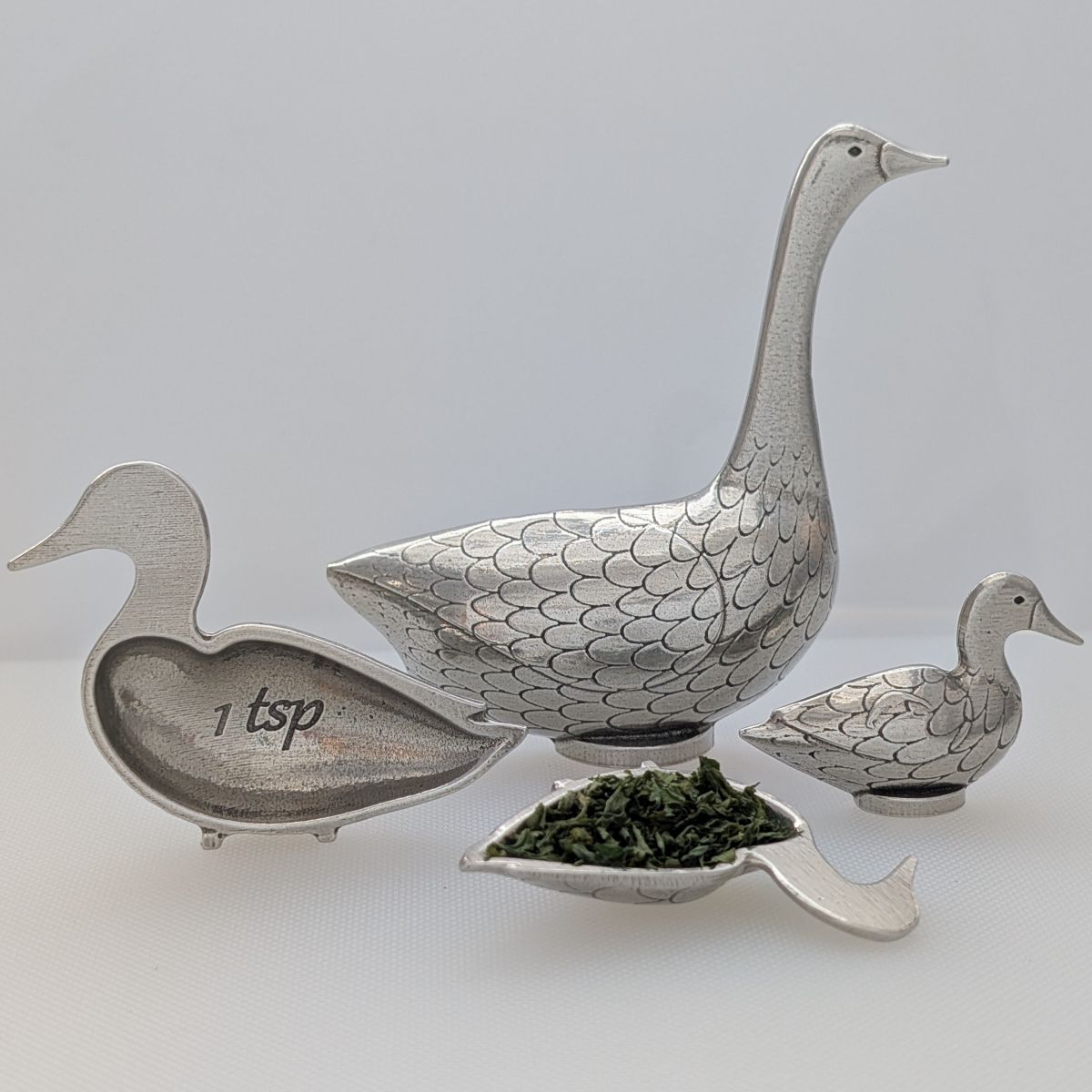 Silver goose-shaped spoon with smaller goose and duck-shaped spoons on a light gray background