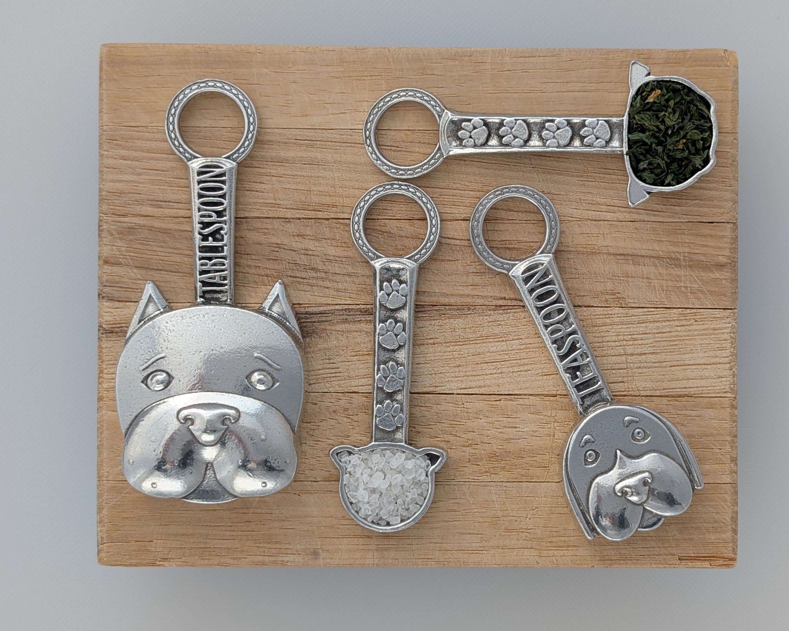 Pewter dog measuring spoons on wood surface