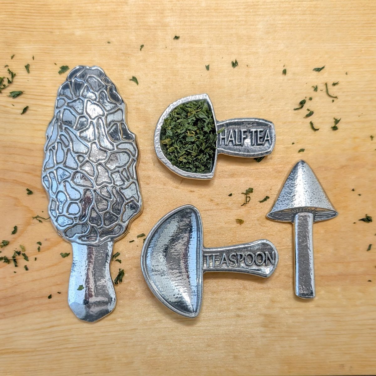 Pewter mushroom measuring spoons on wood with herbs