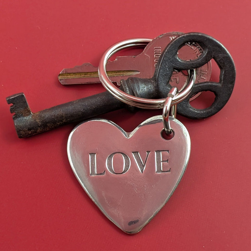 Two keys on a keychain with a heart-shaped tag engraved 'LOVE' against a red background_Roosfoos