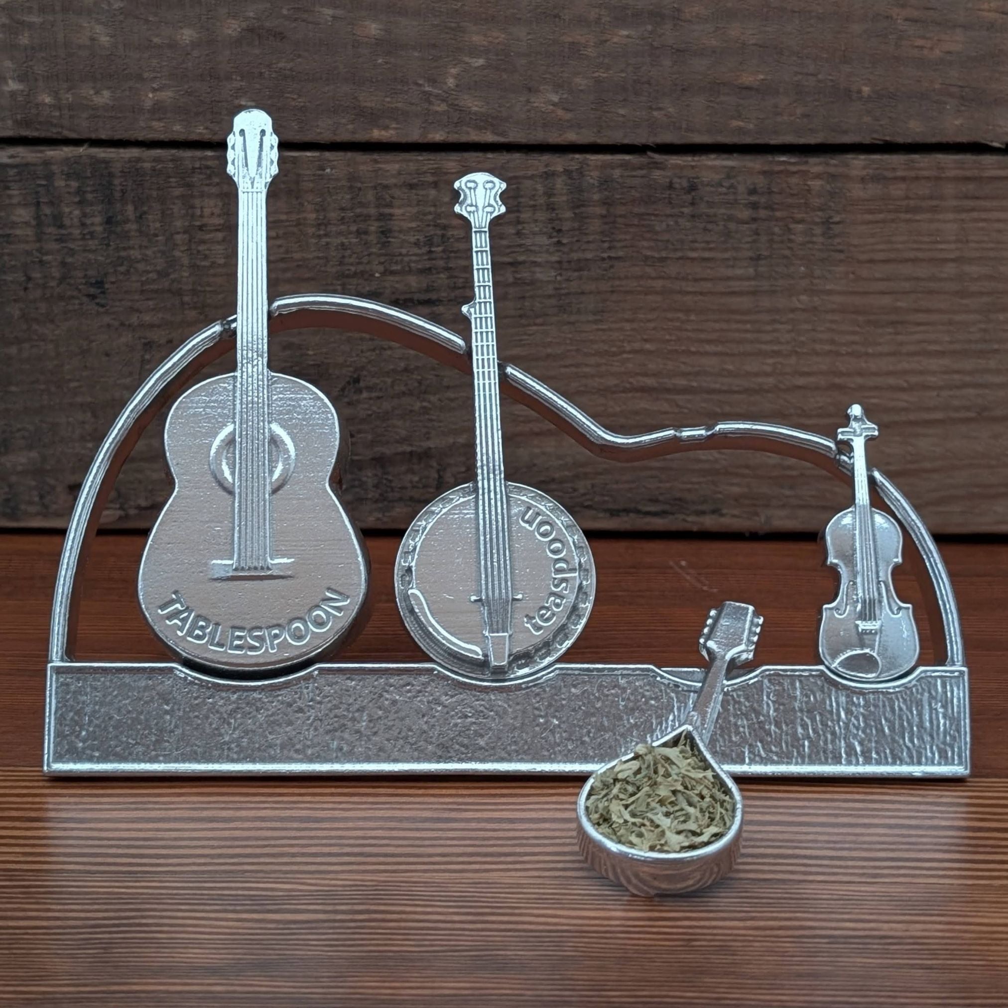 Pewter spoon holder shaped like musical instruments on a wooden surface