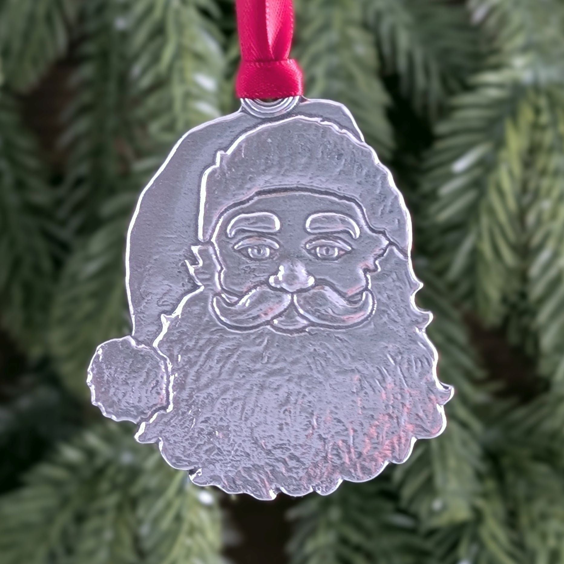 Silver Santa Claus ornament with a red ribbon on a Christmas tree.