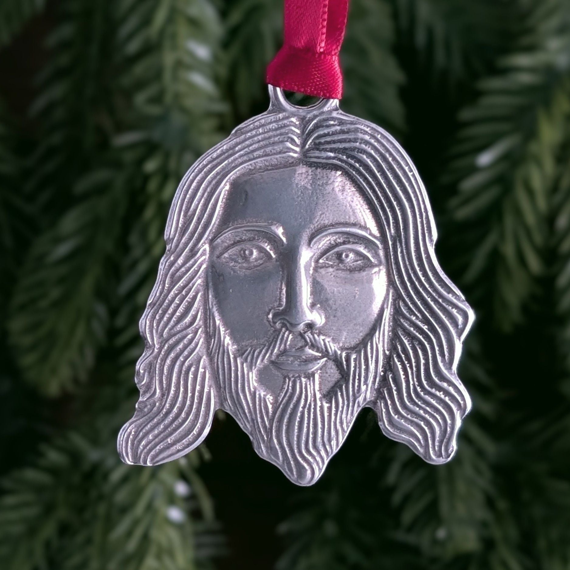 Silver Jesus face ornament with red ribbon on a green Christmas tree