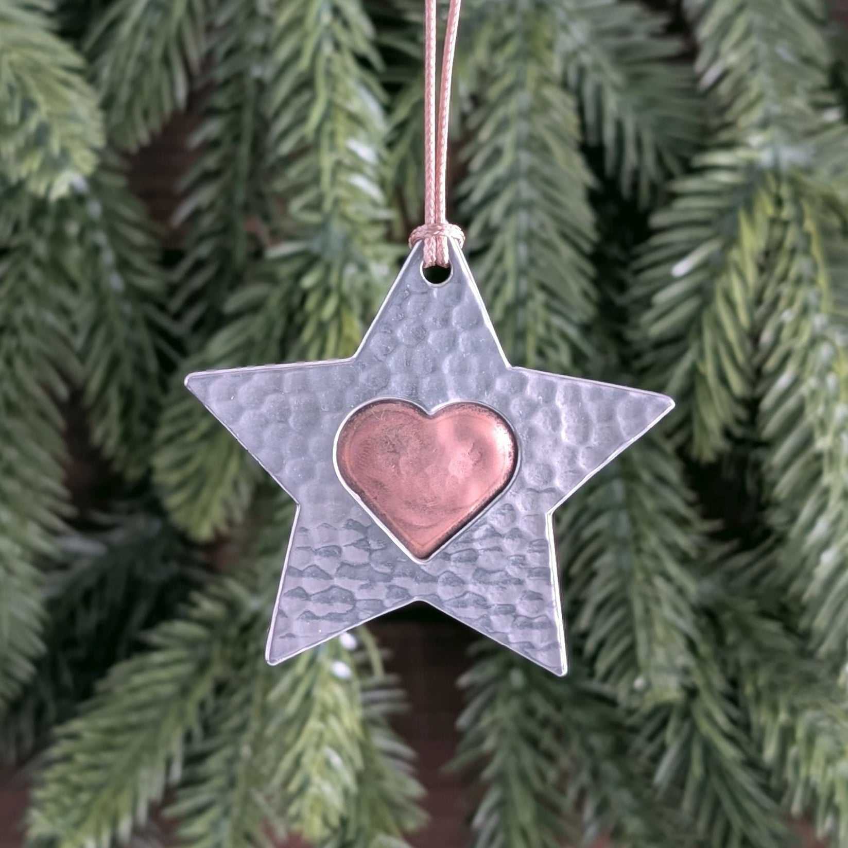 Star-shaped ornament with a heart in the center hanging against a green leafy background