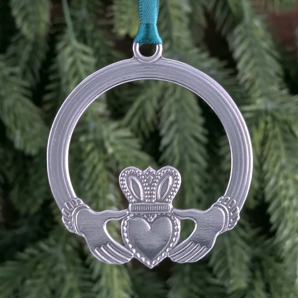 Silver Claddagh ornament with green ribbon against a green foliage background