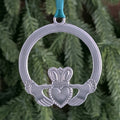 Silver Claddagh ornament with green ribbon against a green foliage background