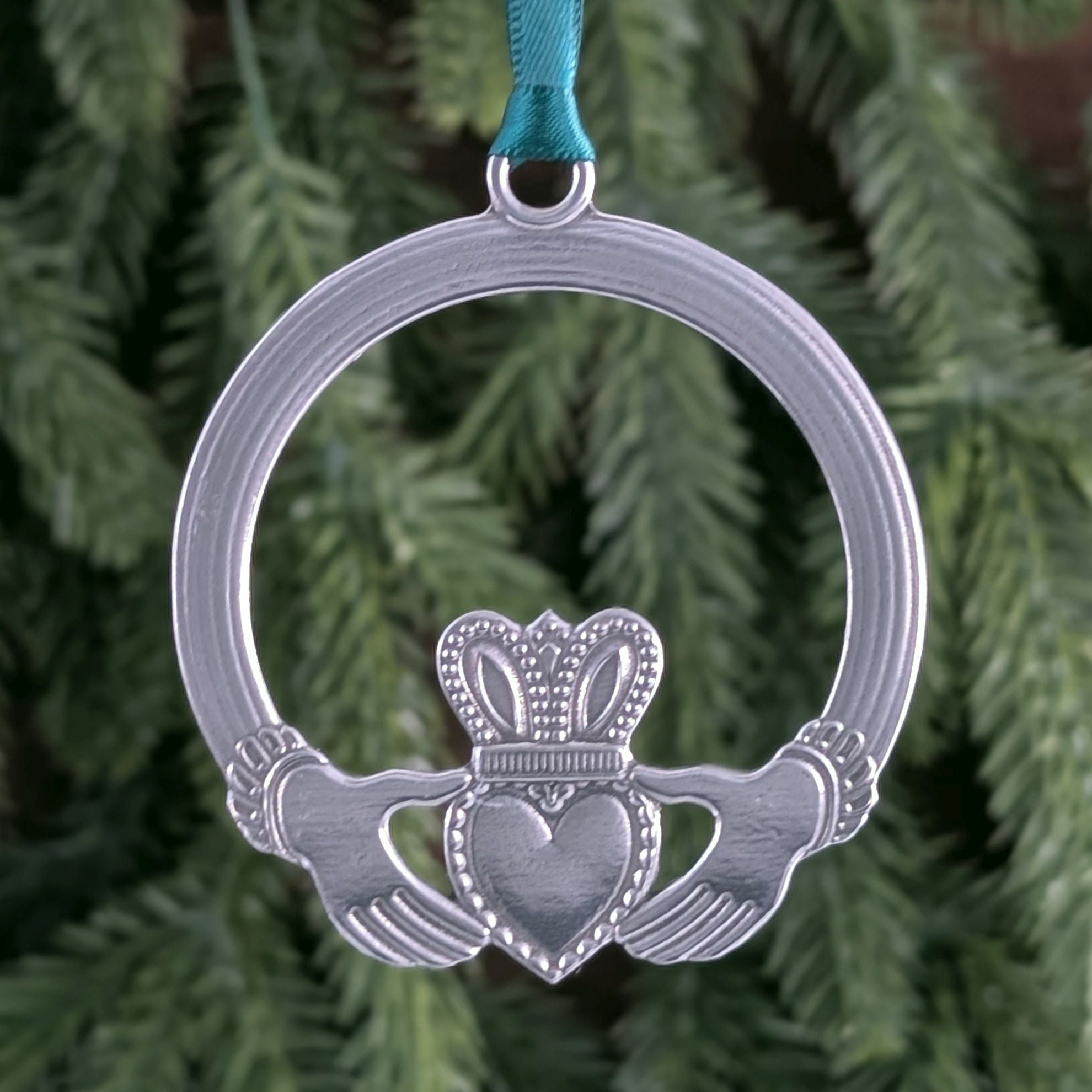 Silver Claddagh ornament with green ribbon against a green foliage background