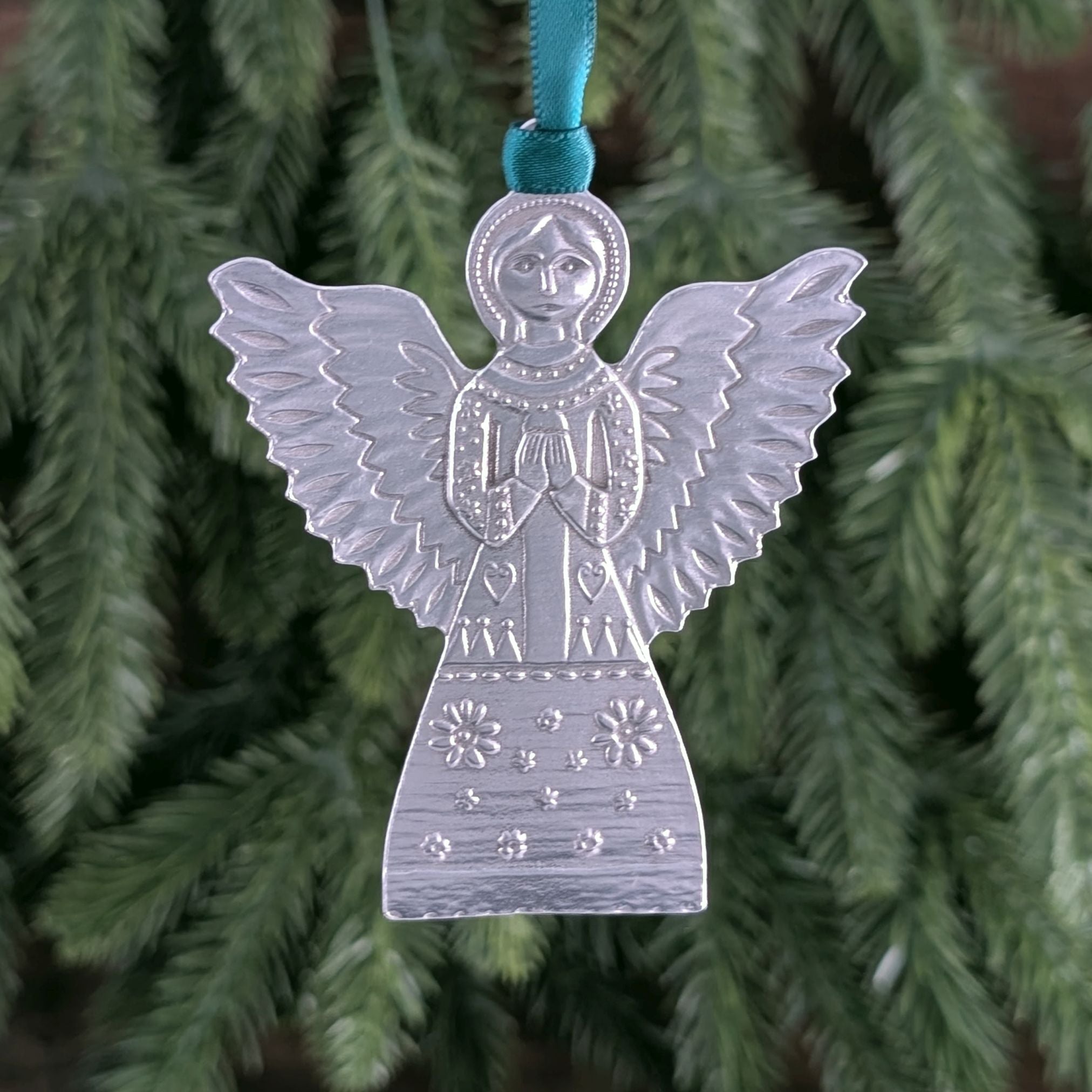 Silver angel ornament with a blue ribbon on a Christmas tree.