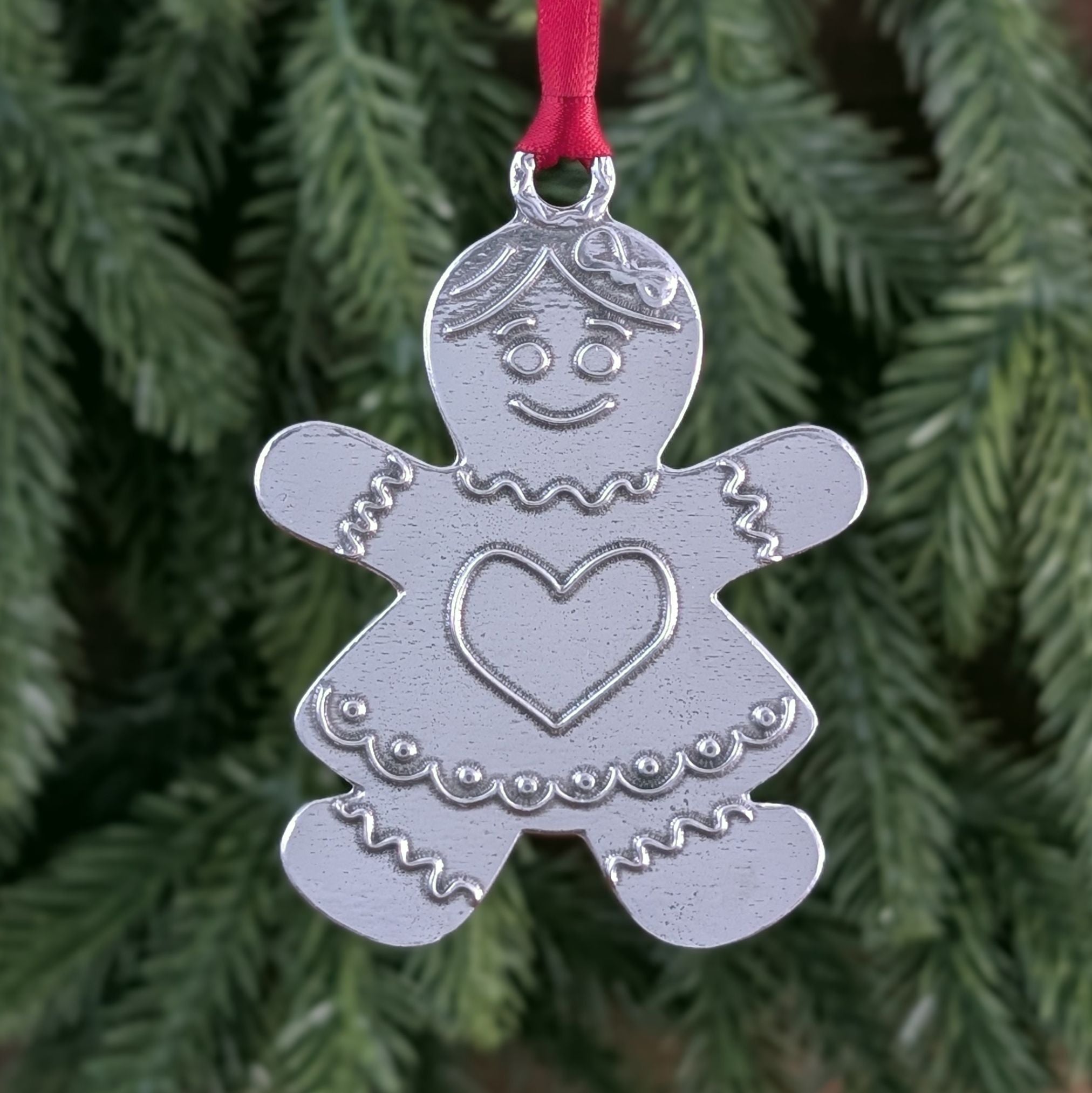 Silver gingerbread woman ornament with a red ribbon on a green Christmas tree.