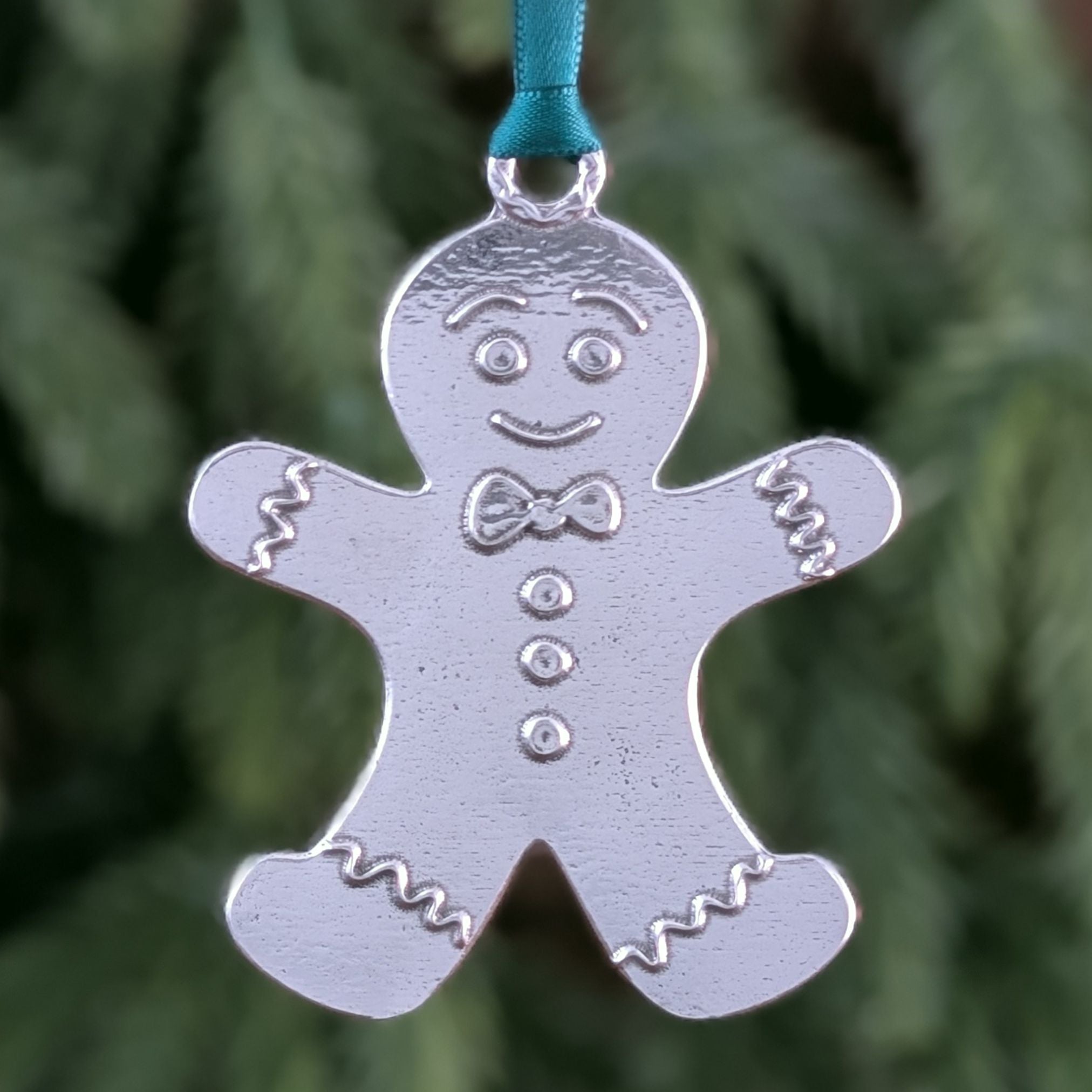 Silver gingerbread man ornament on a green ribbon against a blurred green background