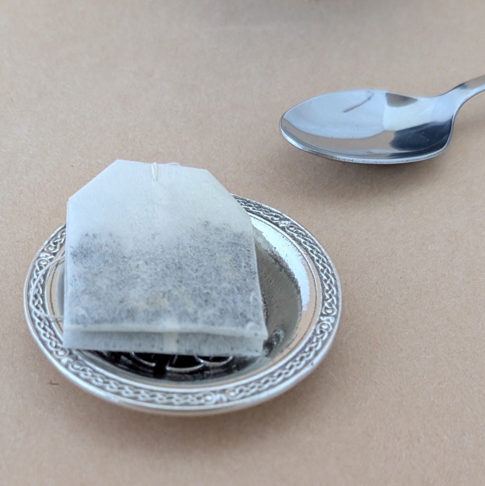 Tea bag on a decorative dish with a spoon on a beige background