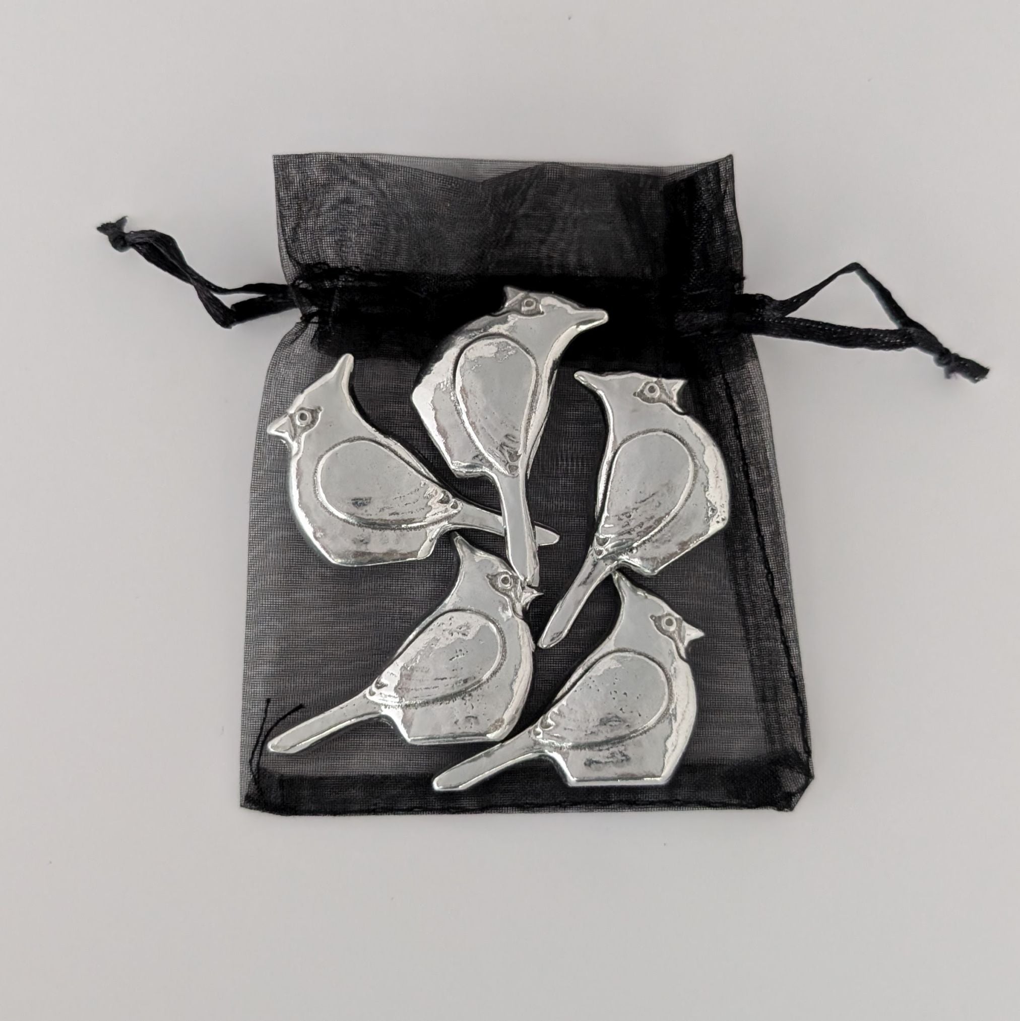 Silver bird-shaped objects in a black drawstring bag on a light gray background